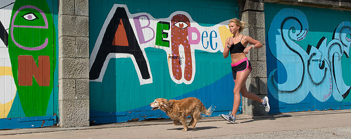 Girl running past the Aberdeen sign on the beach esplanade with her dog